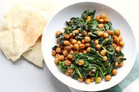 White chickpea and spinach stir-fry in a pan with lemon on the side